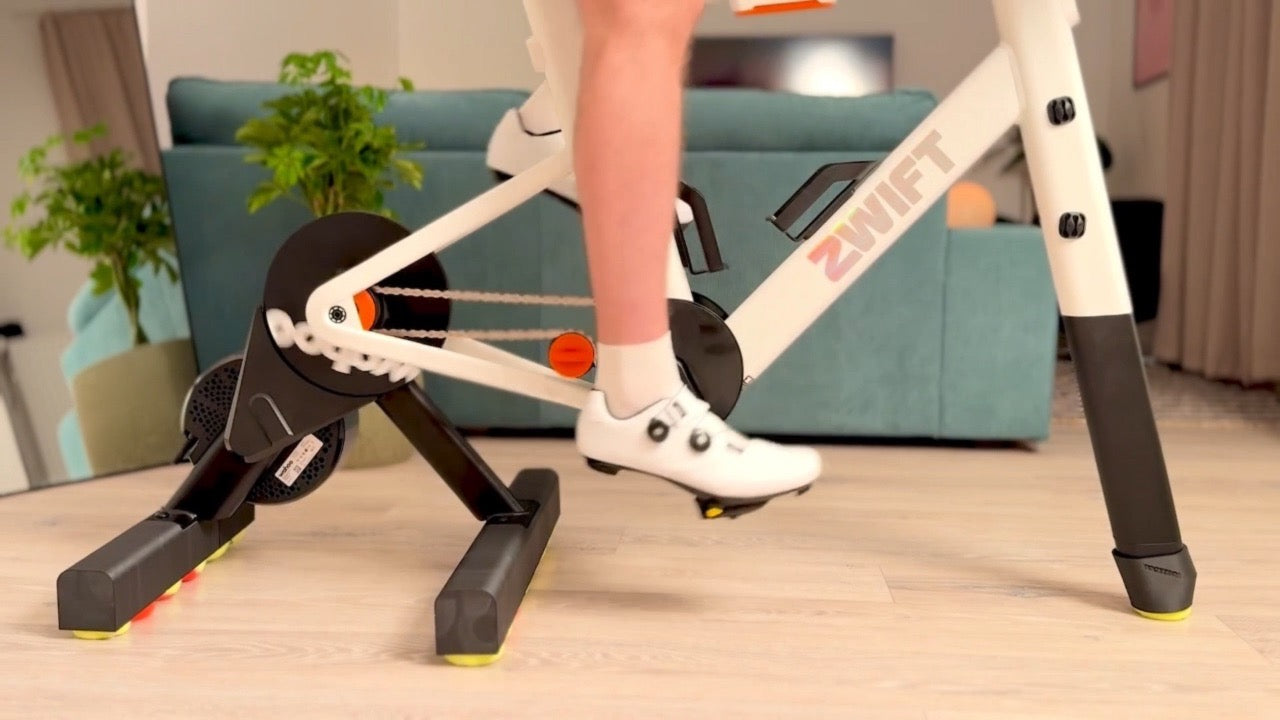 Load video: Side view of a Zwift Ride smart frame mounted on a Wahoo KICKR CORE 2 trainer. ROCKERON adapters with colored balls beneath the trainer and front support enable natural side-to-side movement.